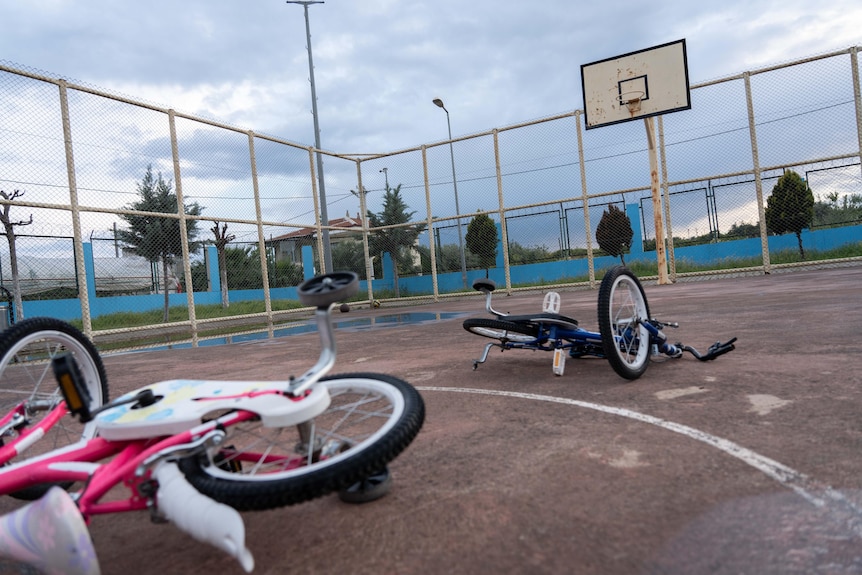 Two children's bikes lay on the ground on a basketball court.