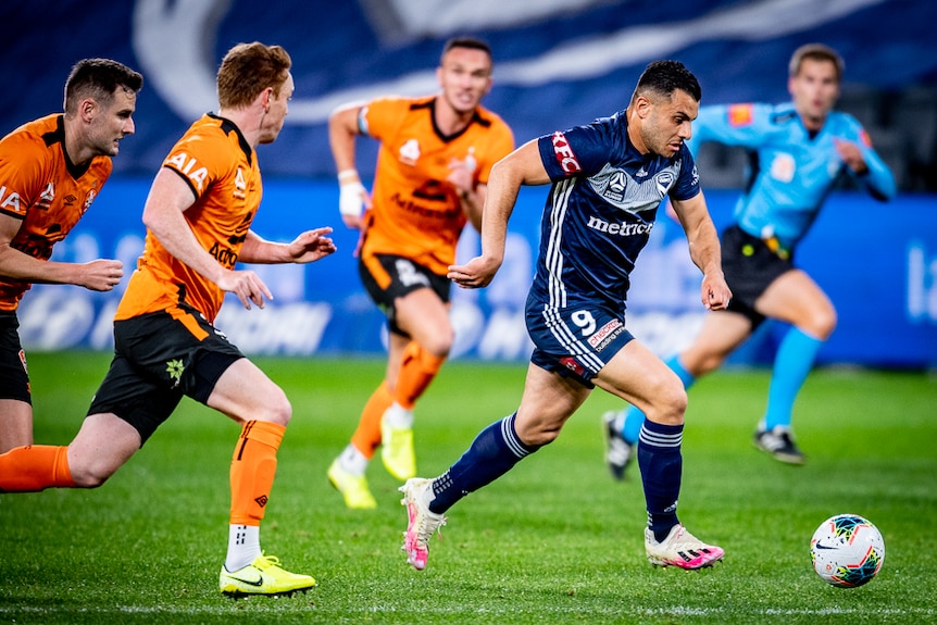 An A-League forward runs with the ball towards goal as he is chased by two opposition defenders.
