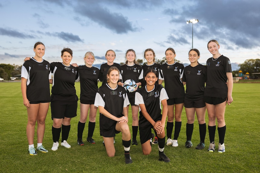 eleven women in all black uniforms pose for group photo on soccer field