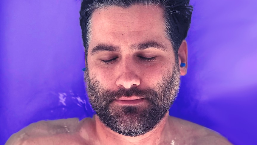 A man's face with ear plugs in and eyes closed, surrounded by water.  For a story on sensory deprivation therapy. 