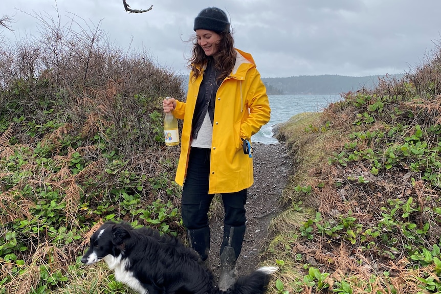 Woman standing outside wearing yellow coat with black and white dog with coastline in background