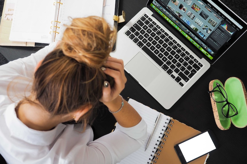 A woman hunches over her desk at work, looking stressed