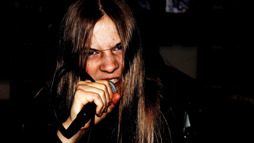 Close up of young man with long hair, grimacing, holding a microphone close to his mouth