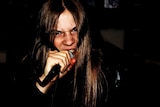 Close up of young man with long hair, grimacing, holding a microphone close to his mouth