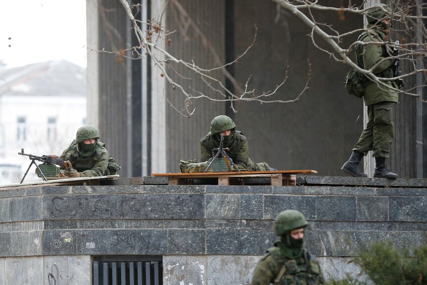 Soldiers in green camouflage, masks and helmets, take up positions with weapons on the roof of a building