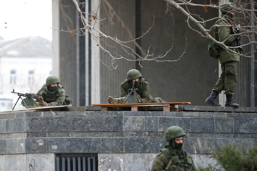 Soldiers in green camouflage, masks and helmets, take up positions with weapons on the roof of a building