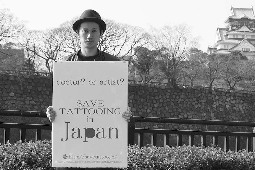 Tatto artist Taiki Masuda. He is standing in front of Osaka Castle, holding a sign for his 'Save Tattooing in Japan' campaign.
