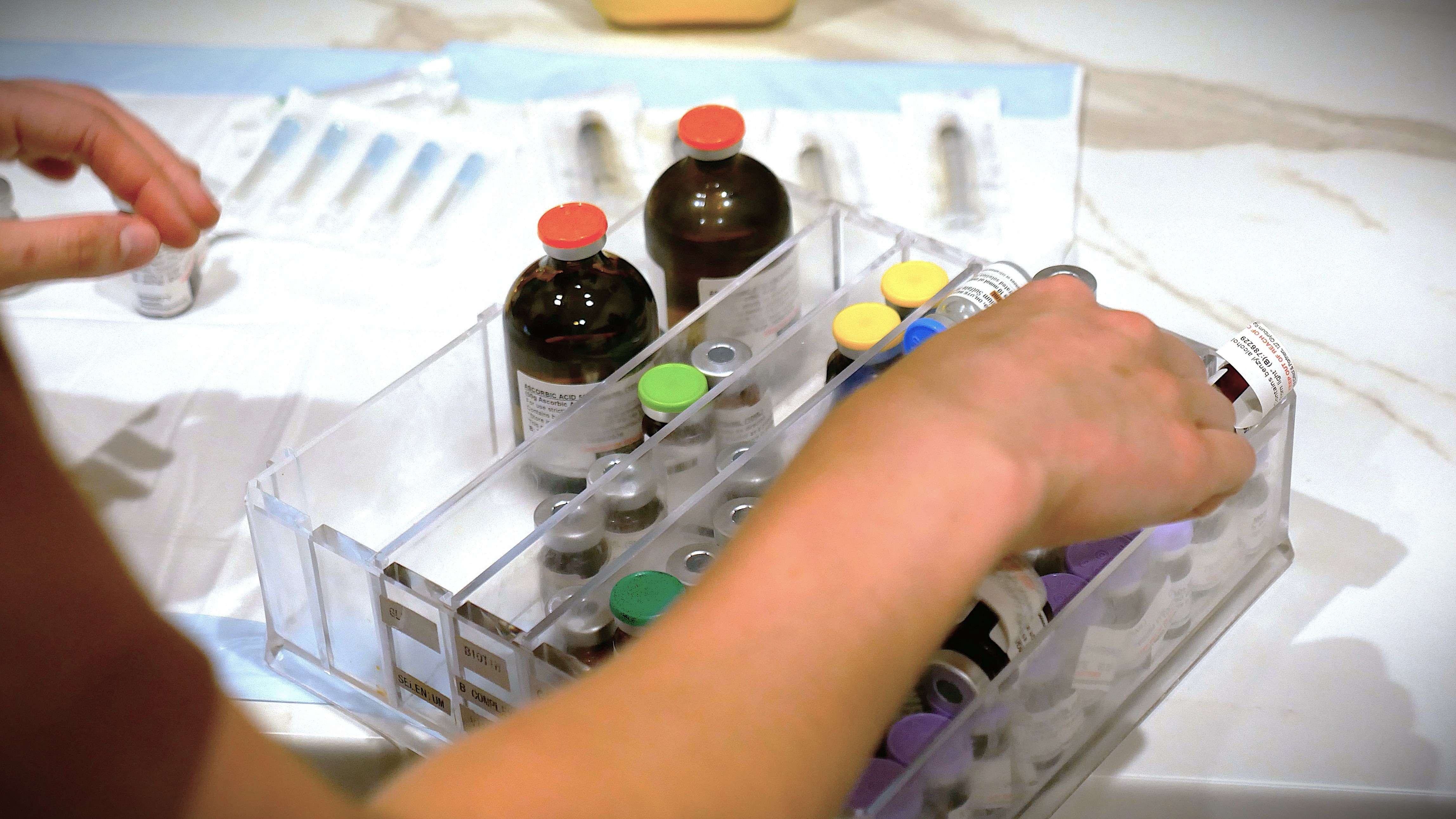A person's hand reaches for a plastic box filled with brown bottles.