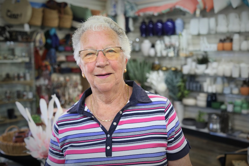 An elderly woman stands smiling in a shop 