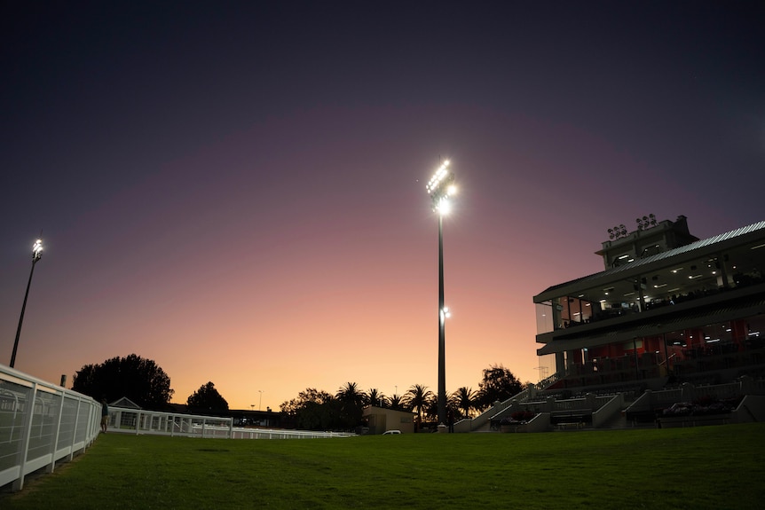 The stand and lights light up at night at a racecourse.