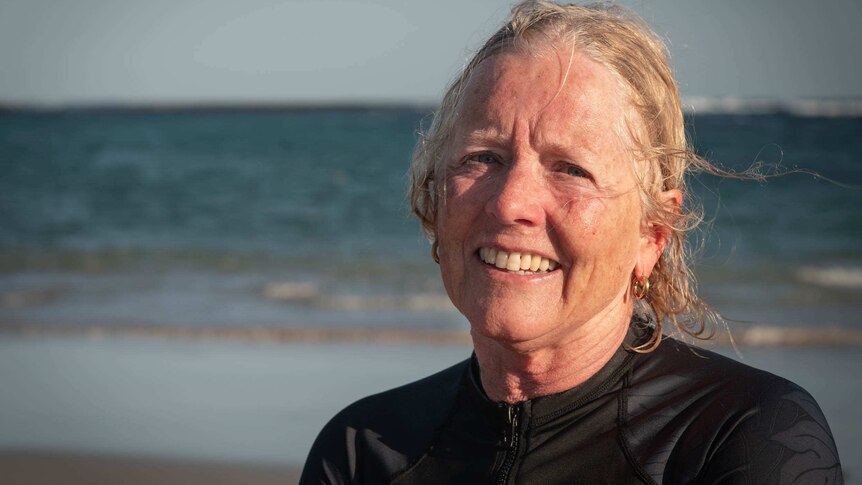 a woman in a wetsuit stares into the camera on the beach