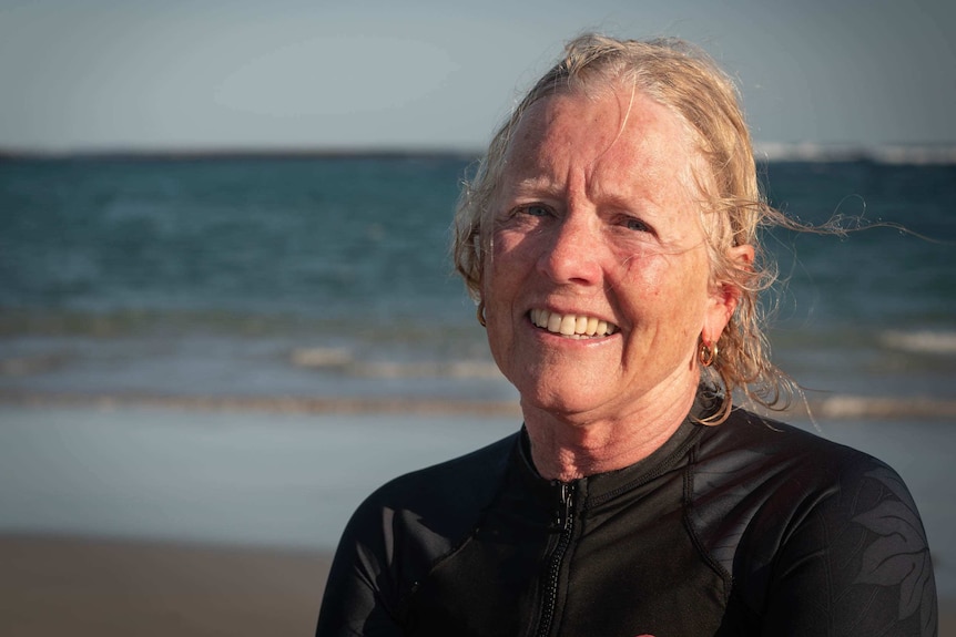 a woman in a wetsuit stares into the camera on the beach