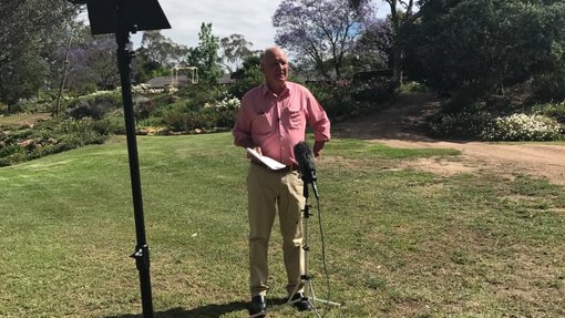 Tony Windsor stands in an open grass patch speaking into a microphone