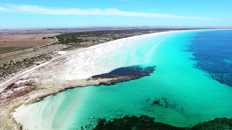 An ocean bay with white sand and turquoise water taken from above.