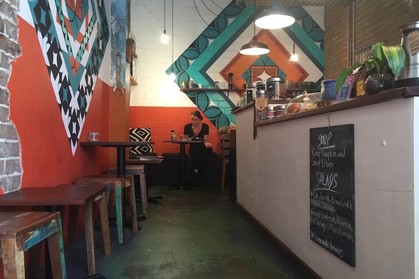 A customer sits at a table at an inner-city cafe with murals on the walls