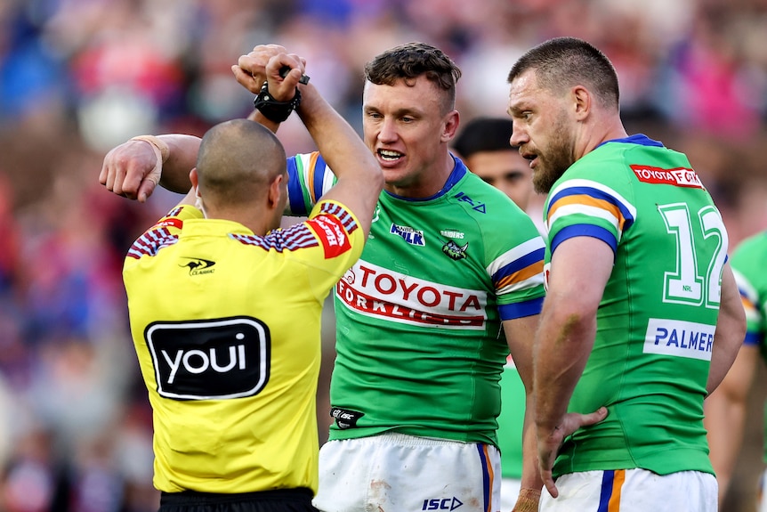 A Canberra NRL player looks at a referee who is holding his hands crossed in an 'X' shape.