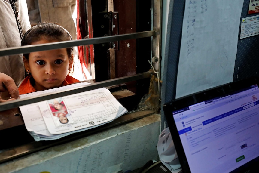 A small girl waits at a window for her ID.