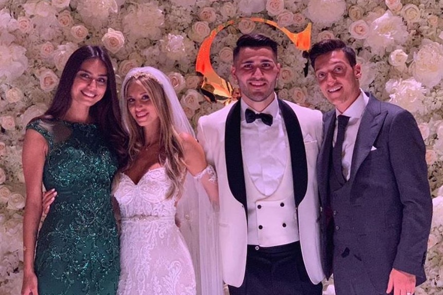 Mesut Ozil (right) and Sead Kolasinac (second from right) stand in front of flowers with two women, one in a wedding dress.