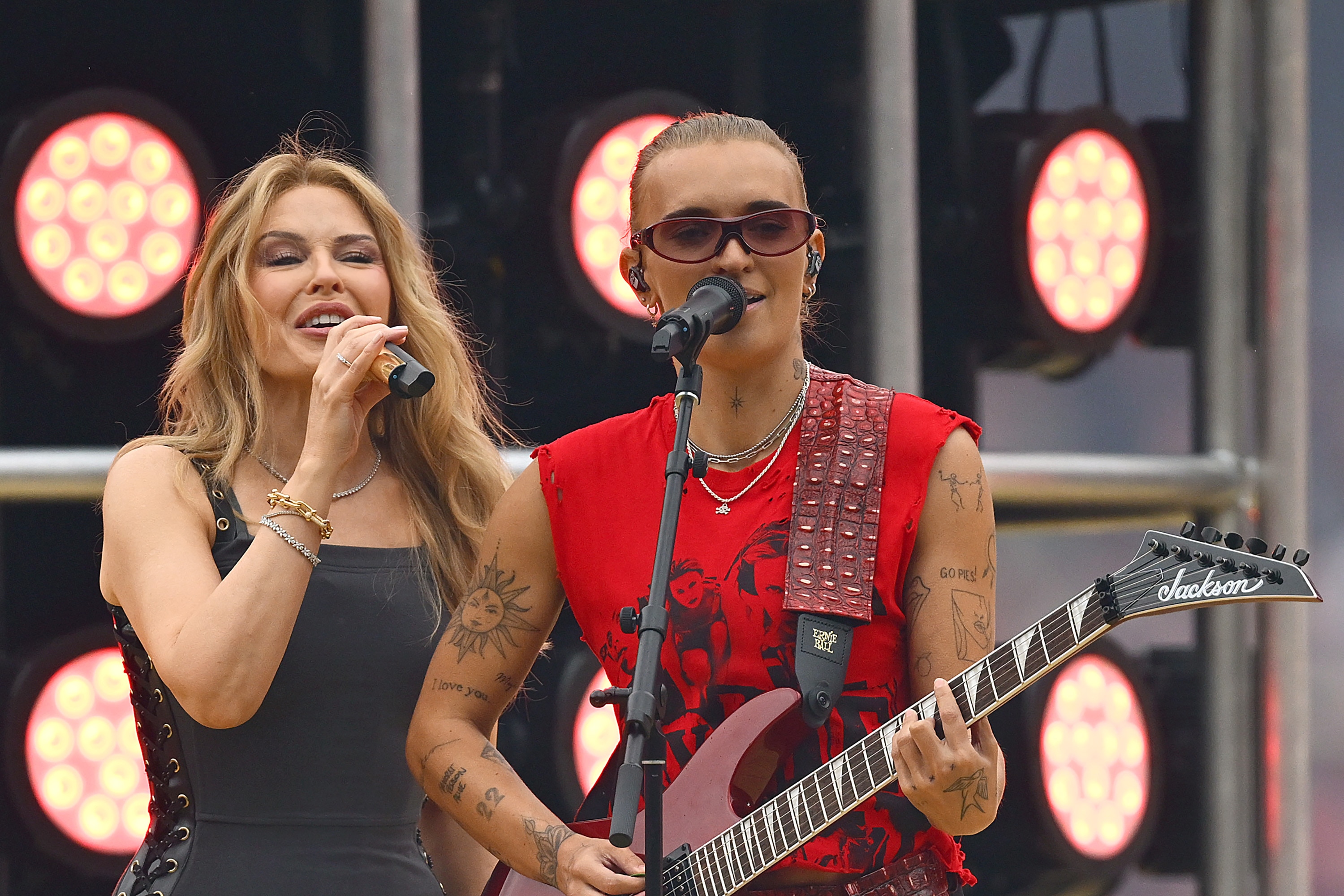 Kylie Minogue wearing black and G Flip wearing red and playing a guitar