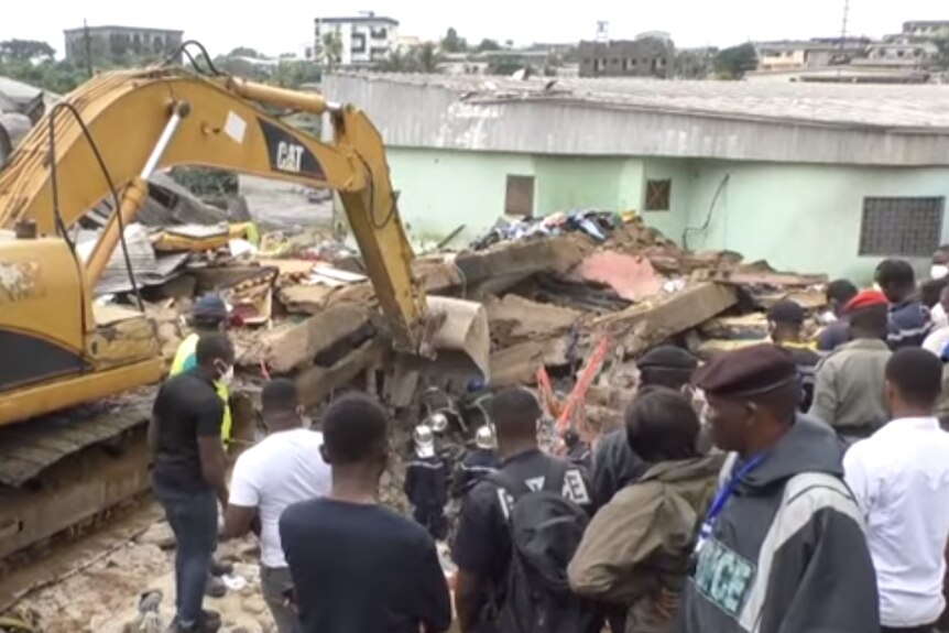 A scene of a collapsed building with an excavator digging through rubble as people watch