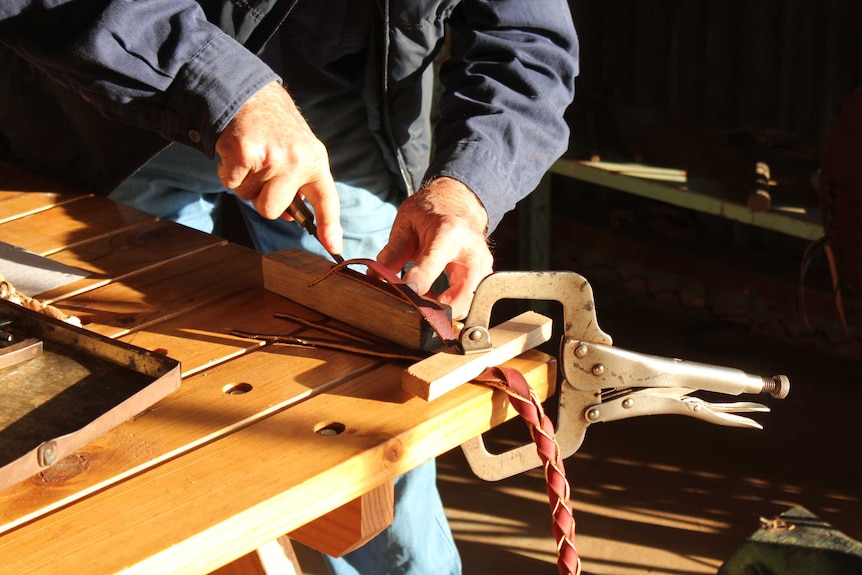 Close up photo of hands cutting a piece of leather on a bench.