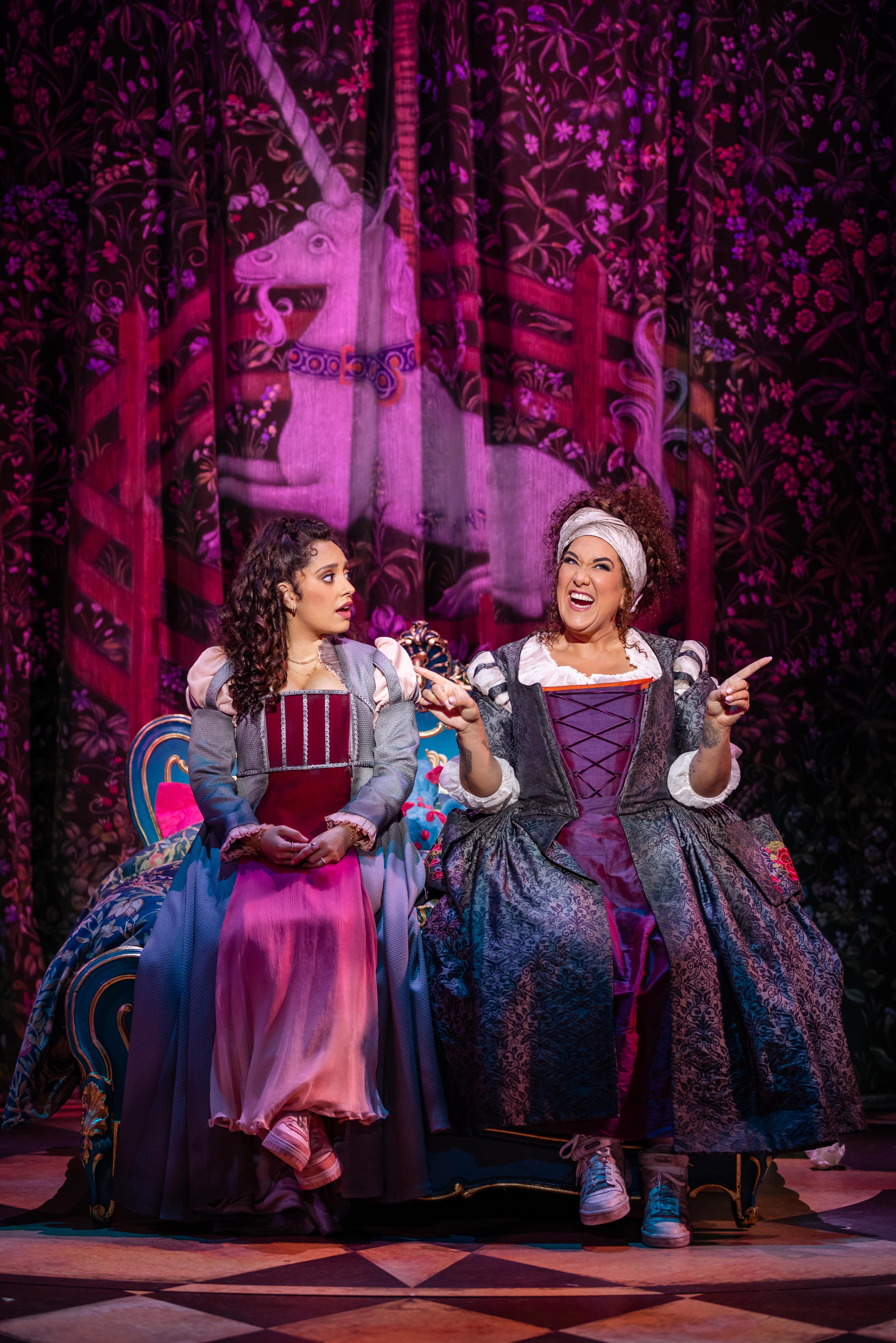 Two women perform on stage, they are dressed in Shakespearean-style clothing. 