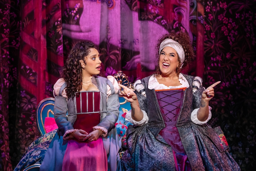 Two women perform on stage, they are dressed in Shakespearean-style clothing. 