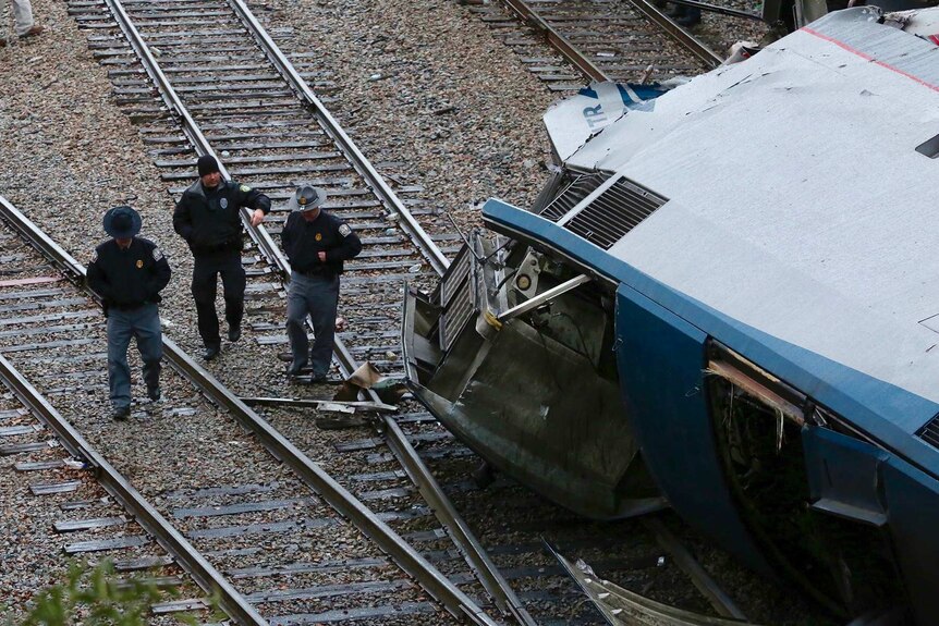 Authorities walk on the tracks near a fallen train carriage.