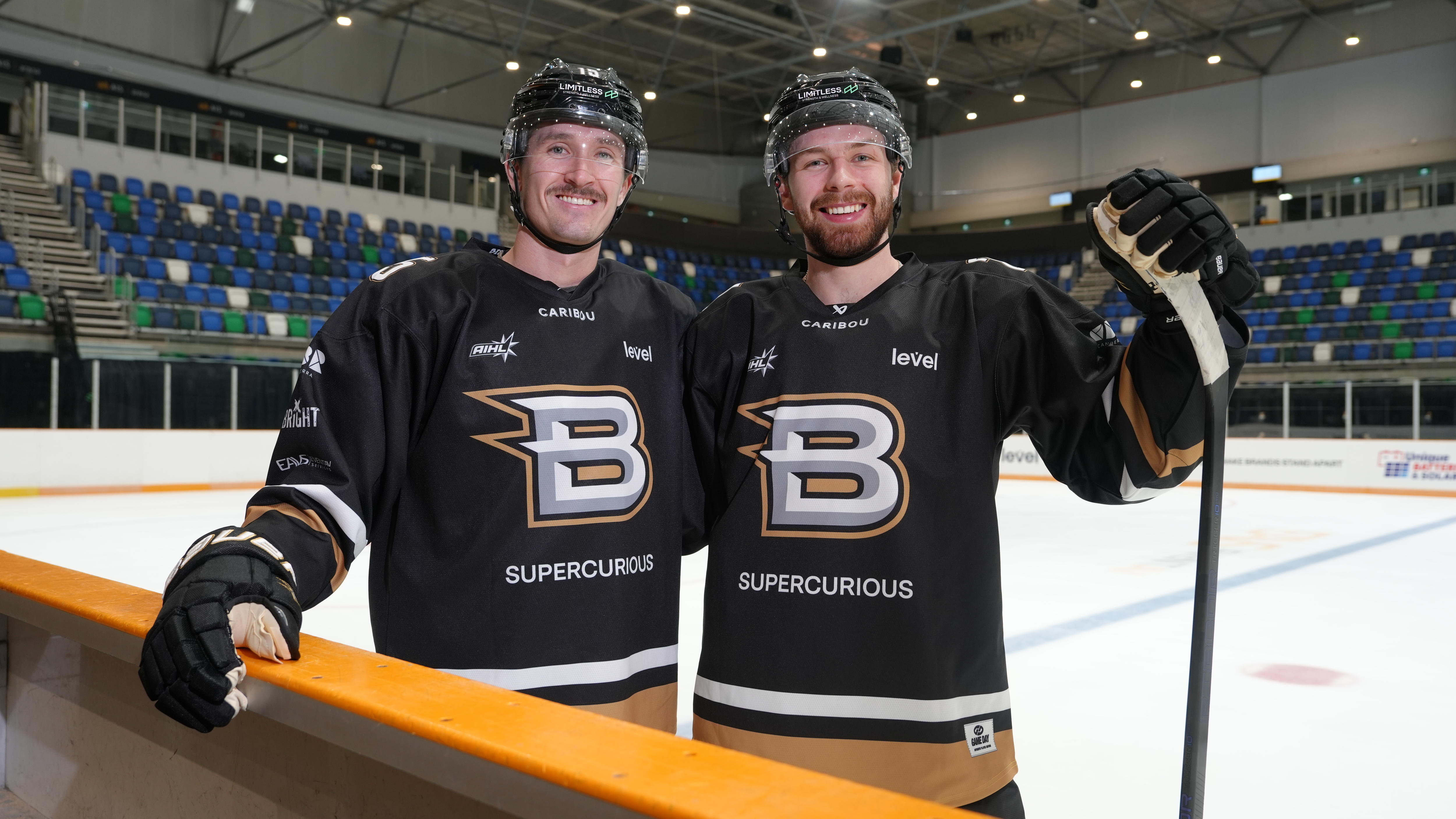 Two people in uniform and helmets holding hockey sticks stand on an ice rink.