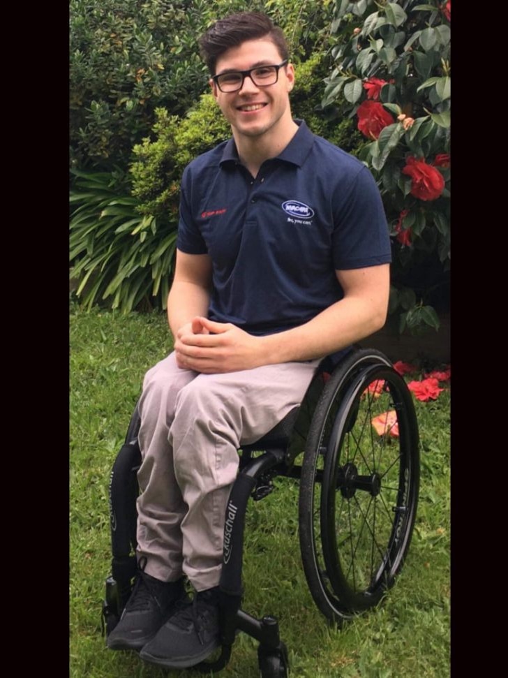 A man sits in a wheelchair smiling.