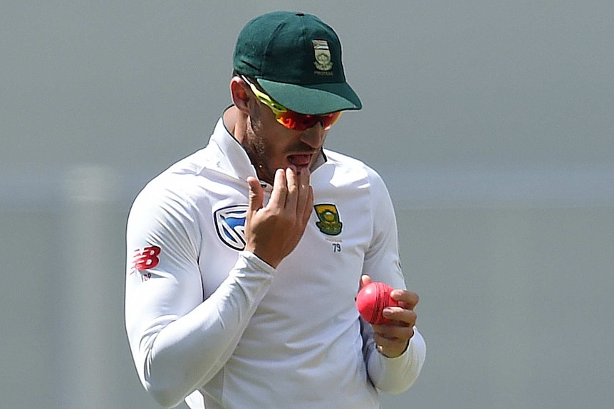 Faf du Plessis licks his fingers to shine a cricket ball during a Test match.