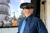 Doug Bester wears a 3D iPhone virtual reality mask. A worker in high viz works in the background.