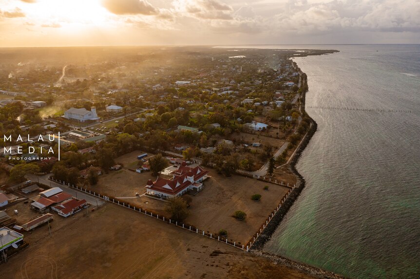 Aerial image of main buildings in Tonga next to ocean as sun sets. 
