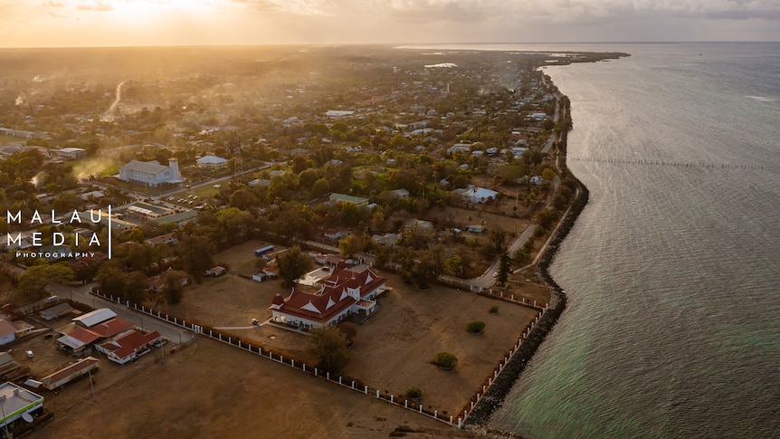 Aerial image of main buildings in Tonga next to ocean as sun sets. 