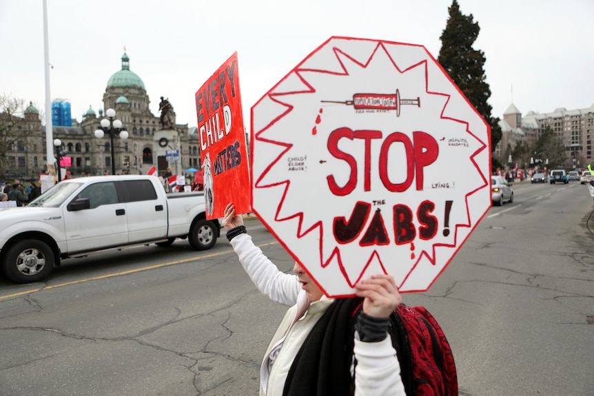 An anti-vaccine protester holds a placard reading 'stop jabs'