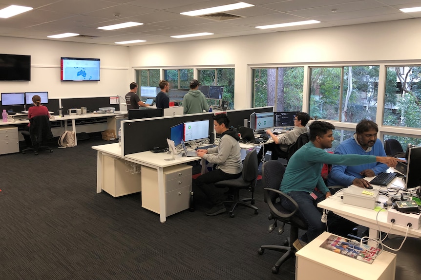 an office floor with workers and computer screens