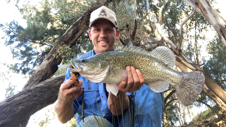 A man in a cap smiles and holds up a big fish.