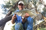 A man in a cap smiles and holds up a big fish.