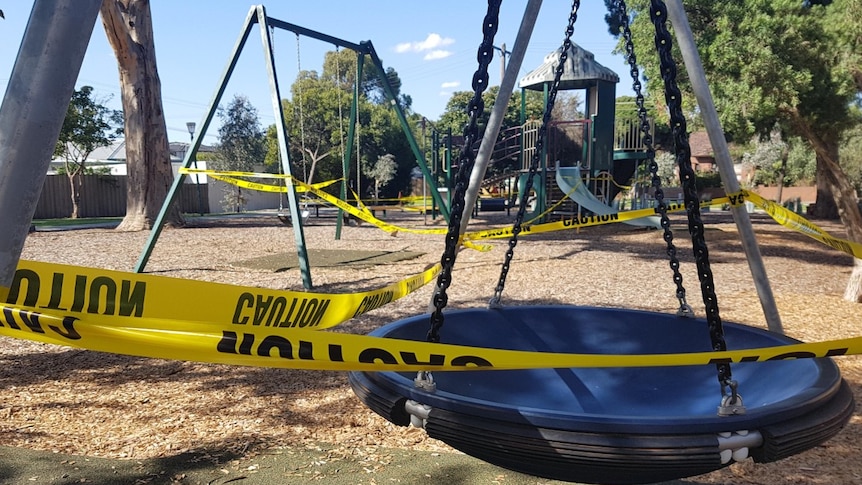 Yellow tape is wrapped around children's play equipment in a suburban park.
