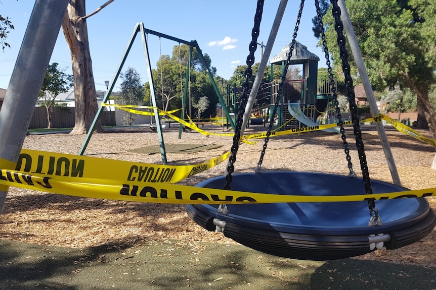Yellow tape is wrapped around children's play equipment in a suburban park.