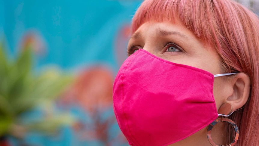 A close up image of a woman wearing a bright pink cloth face mask.