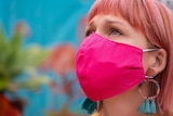 A close up image of a woman wearing a bright pink cloth face mask.