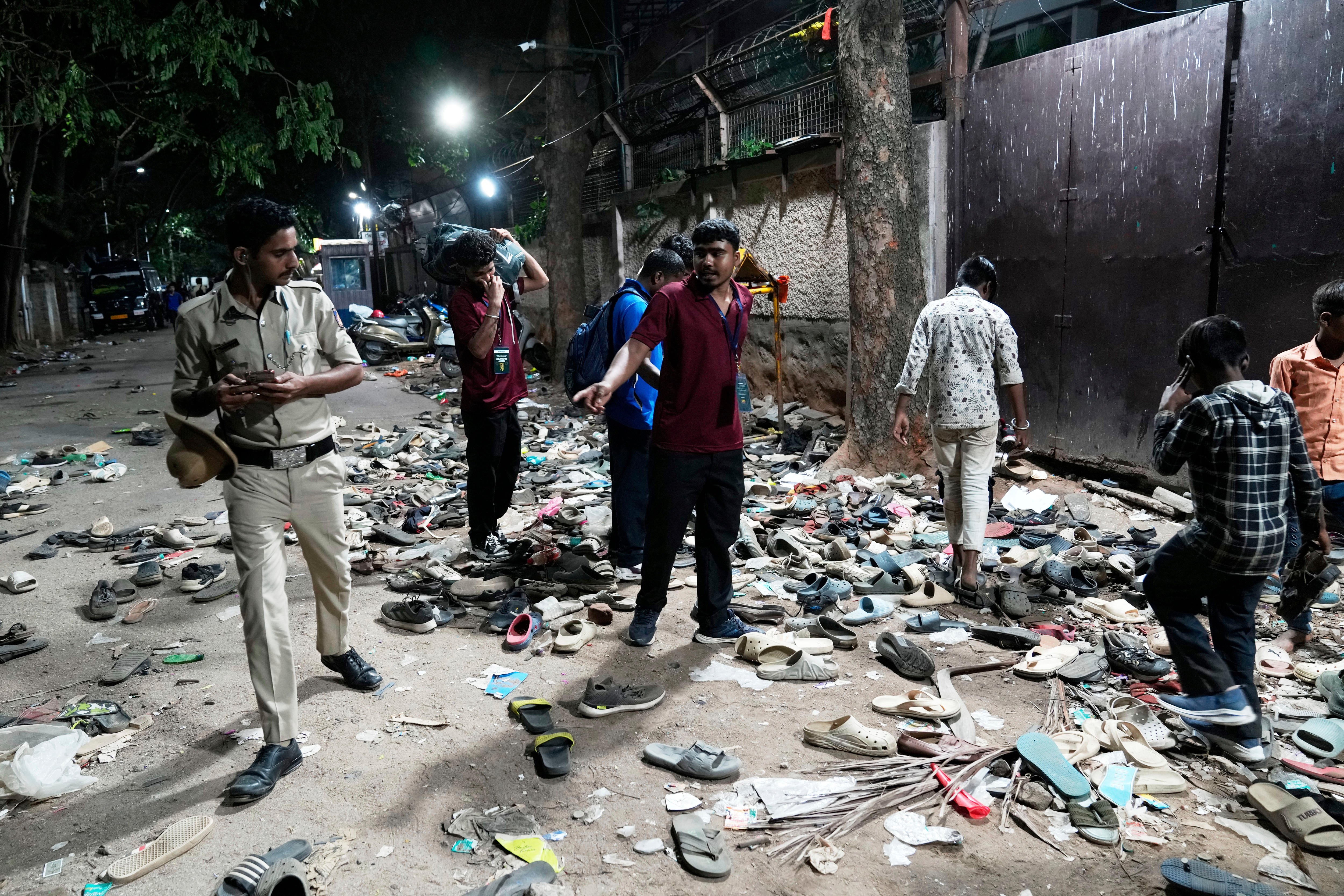 Men and children alongside a police officer walking on piles of empty shoes on a dusty roadway alongside a fenceline