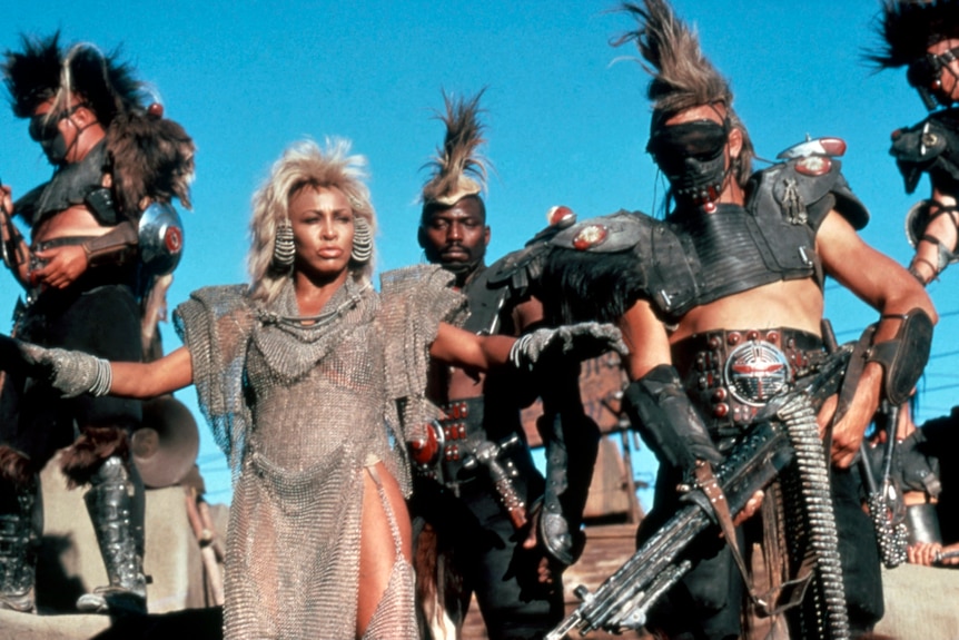 A screenshot shows Tina Turner as Auntie Entity in a mesh outfit, spreading her arms in front of followers.