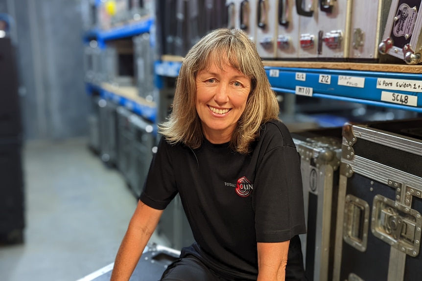 Natalie Peterson sits on a music equipment box smiling at the camera. 