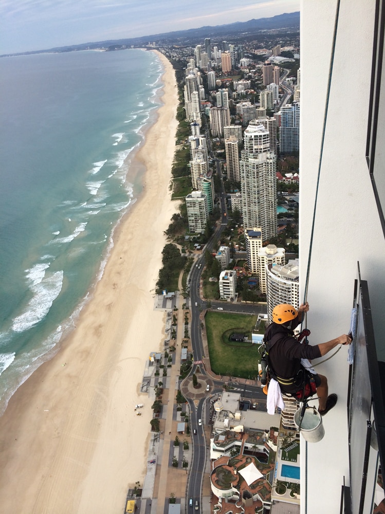 An abseiling cleaner hangs from the side of a Gold Coast building