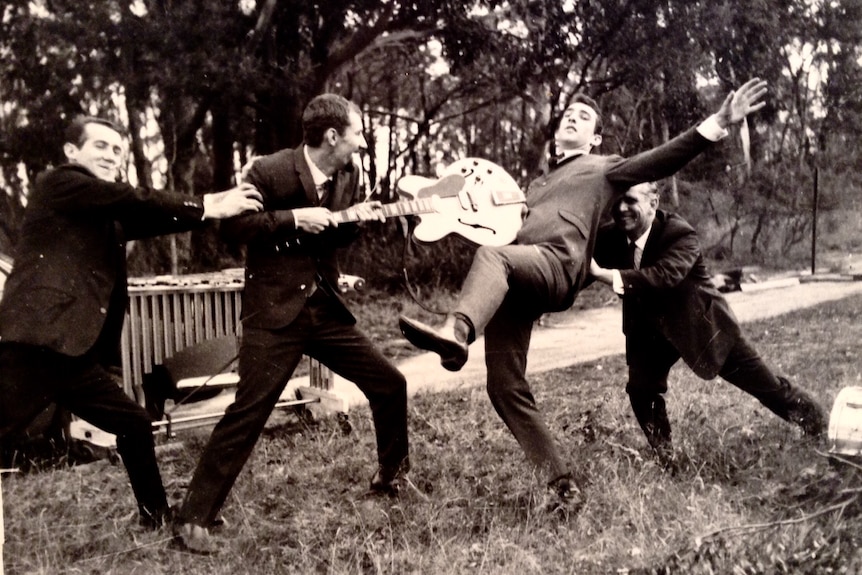 Four band members in suits horse around with each other in an outdoor setting
