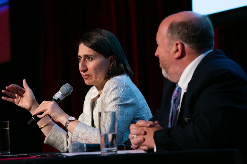 Two people sit as if at a public forum.