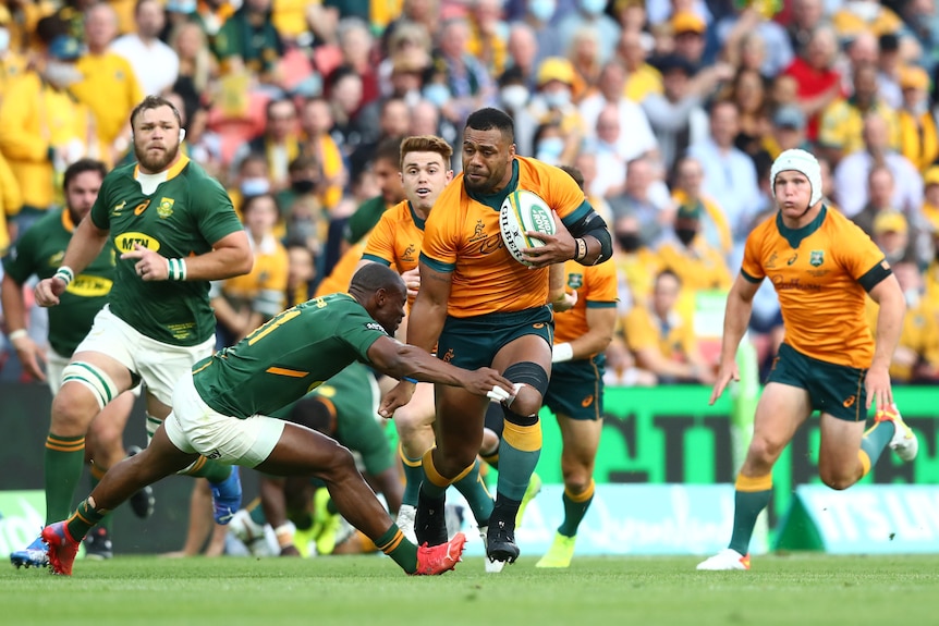 A Wallabies player runs with the ball as the Springboks attempt to tackle him.