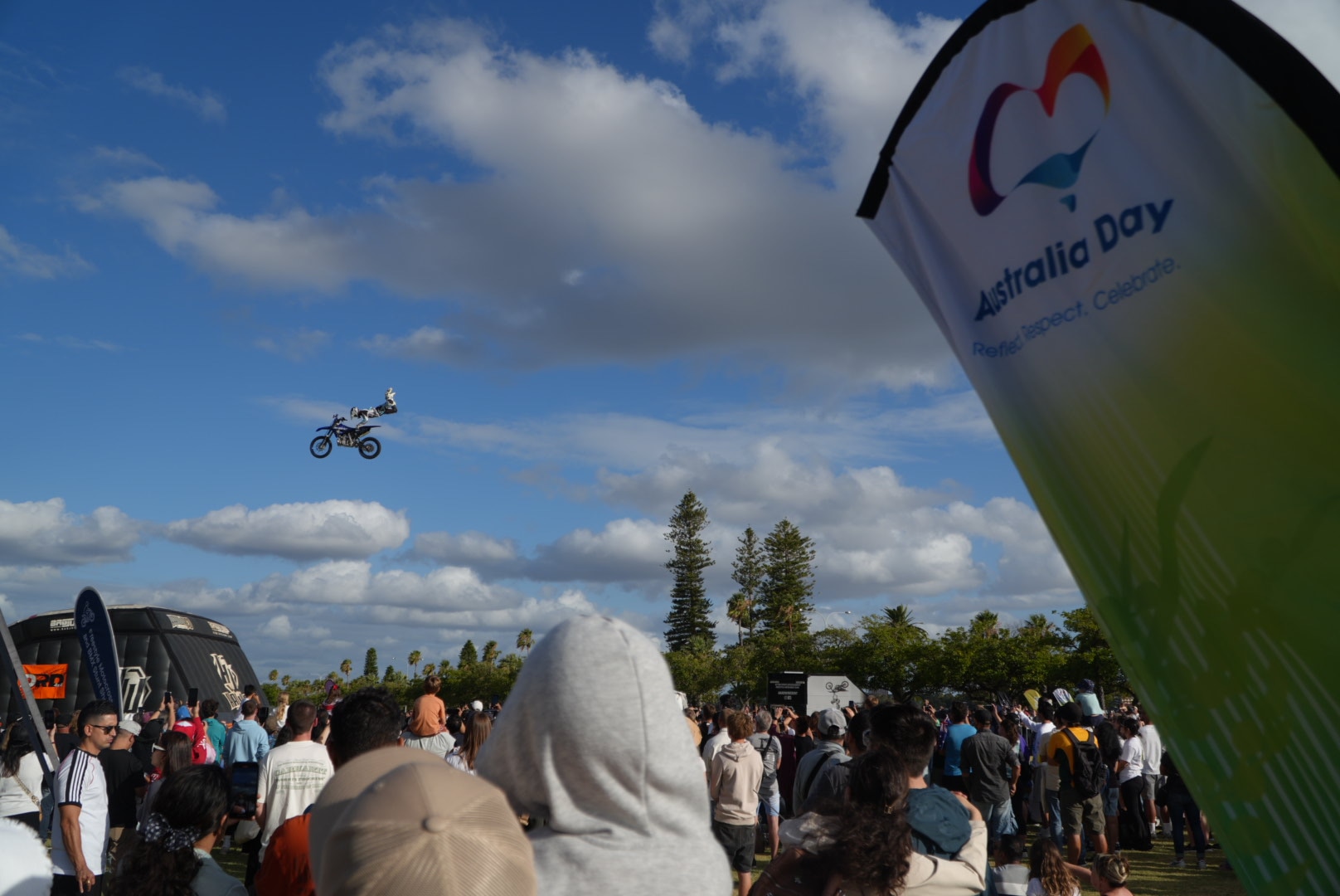 Un ciclista de BMX vuela por el aire a lo lejos, encima de una multitud de personas y un cartel que dice 